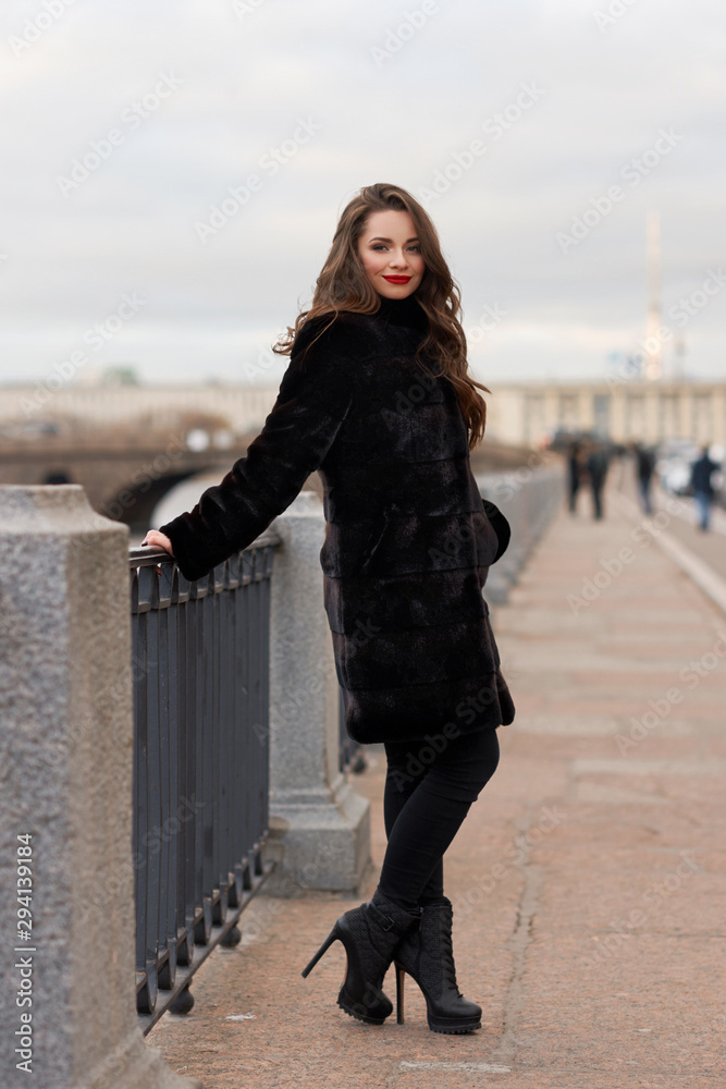 Fashion photo of young gorgeous beautiful woman in black fur coat at city street