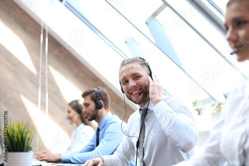 Portrait of call center worker accompanied by his team. Smiling customer support operator at work. © ty