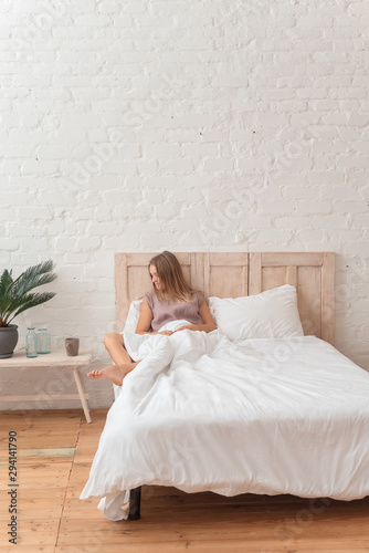 beautiful girl lying in her bed and drinking morning tea, bedroom in loft style