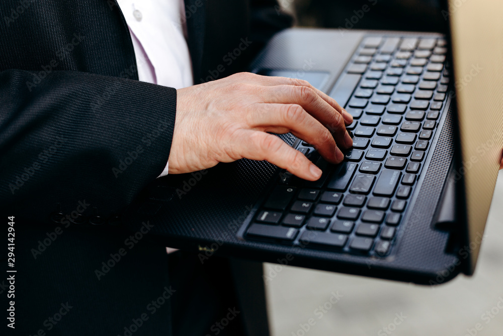 Cropping image of senior businessman holding laptop in his hand and typing closeup.- Image Cropping image of senior businessman holding laptop in his hand and typing closeup.- Image
