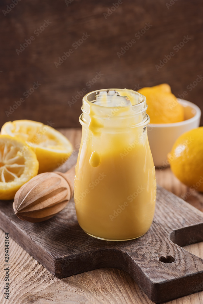 Lemon curd in a glass jar, cutting lemon on a wooden background, ingredients for cooking, lemon kyrd recipe