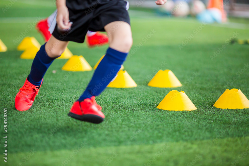 Kid soccer player putting red sport shoes to jogging between yellow marker cones on green artificial turf for soccer training of academy. Kid soccer player putting red sport shoes to jogging between yellow marker cones on green artificial turf for soccer training of academy.