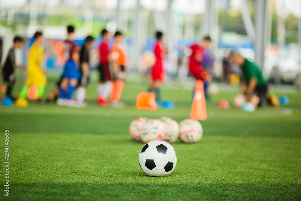 Soccer ball on green artificial turf with blurry soccer team training. Blurry kid player training and soccer equipment in soccer academy. Soccer ball on green artificial turf with blurry soccer team training. Blurry kid player training and soccer equipment in soccer academy.