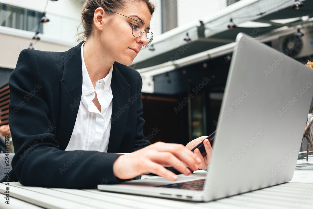 Young business woman wearing glasses at cafe using laptop and. Businesswoman sitting at coffee shop on terrace and working on computer Young business woman wearing glasses at cafe using laptop and. Businesswoman sitting at coffee shop on terrace and working on computer