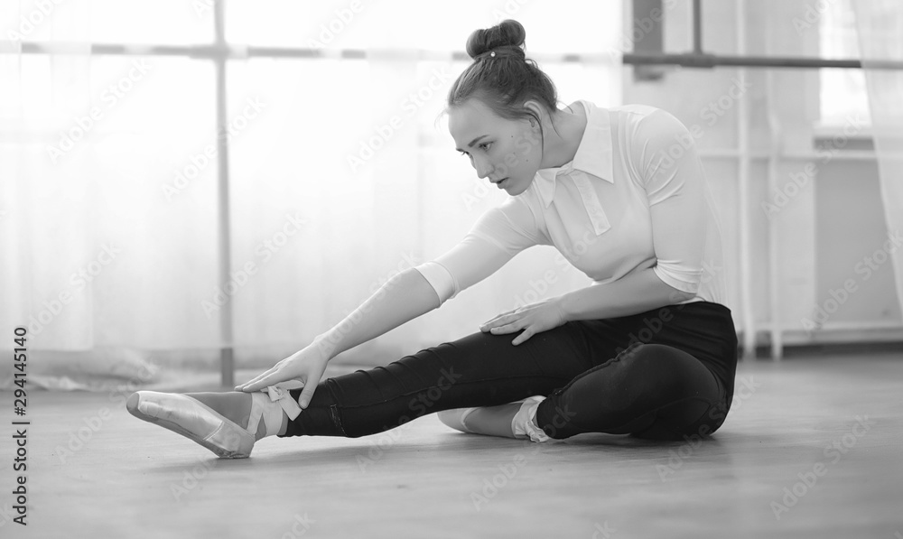 Fototapeta premium Young ballet dancer on a warm-up. The ballerina is preparing to perform in the studio. A girl in ballet clothes and shoes kneads by the handrails.
