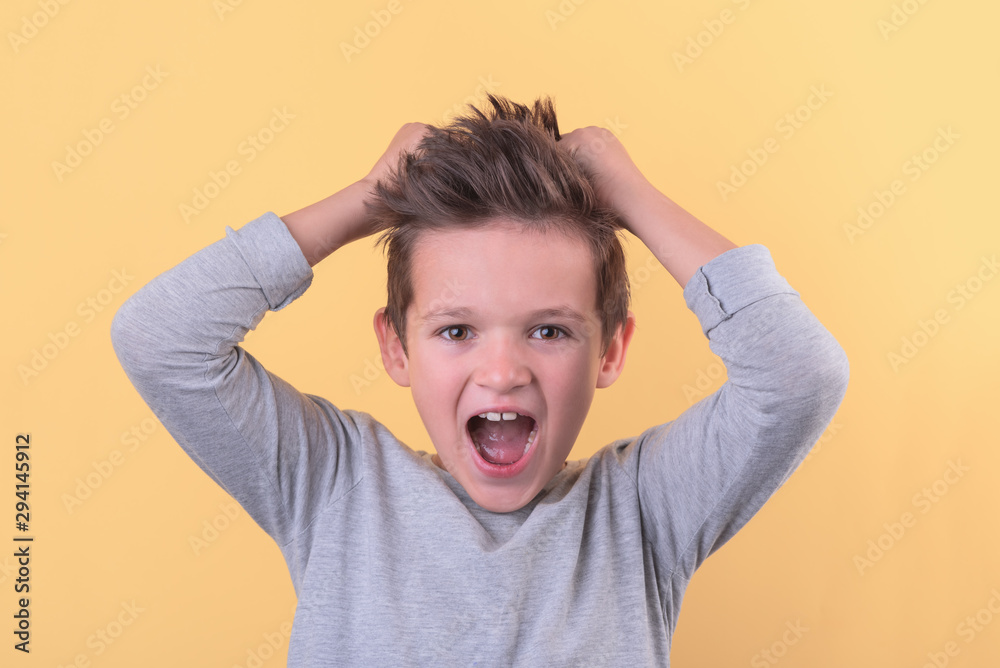 Handsome boy holds two hand on head and scream over yellow background, the concept of children's emotions