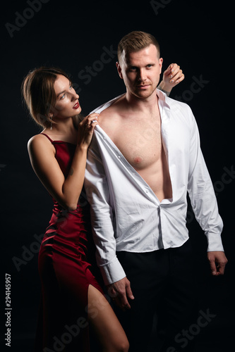 charming sexy girl takes care of her strong muscular boyfriend. close up portrait, isolated black background, studio shot