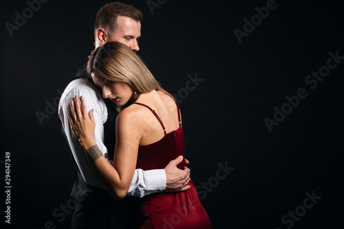 young elegant man supports his woman, embracing her. close up portrait, isolated black background, studio shot. separation. I love you,. miss you. copy space