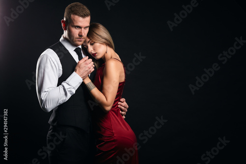 serious strong man protects his week slim elegant woman. close up portrait, isolated black background, studio shot.copy space.