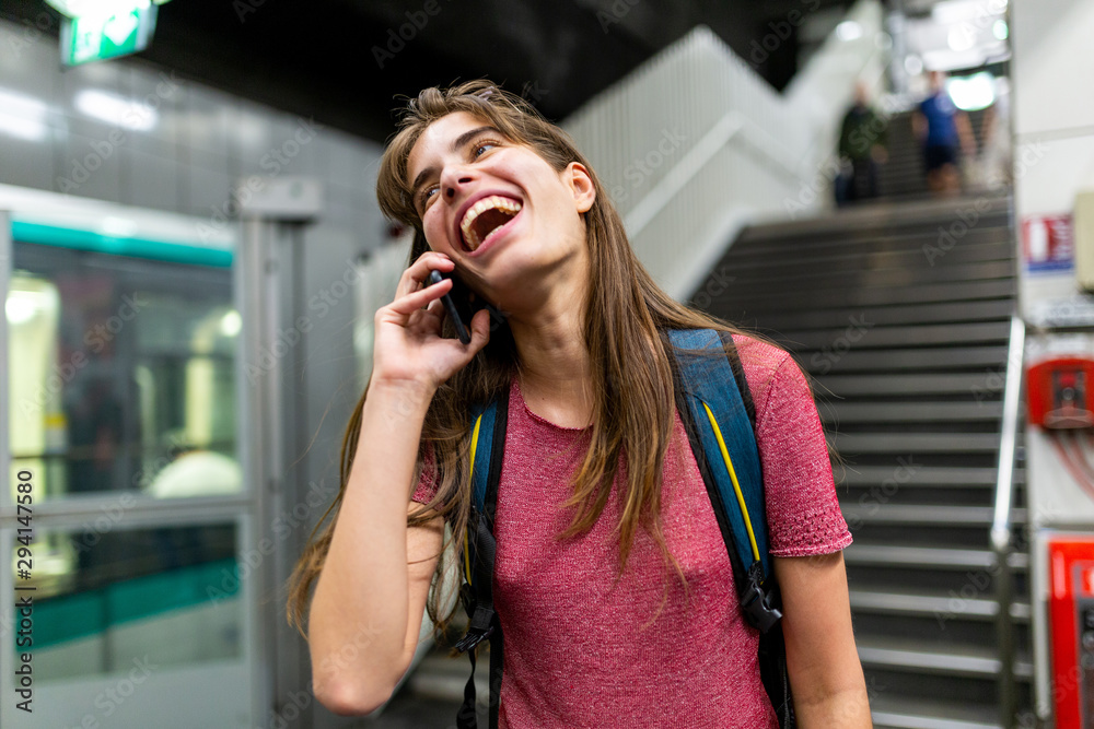 Fototapeta premium happy young woman talking on mobile phone in underground station and laughing
