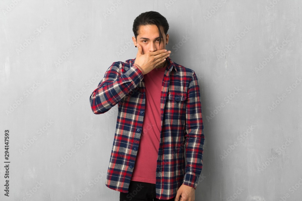 Man over grunge wall covering mouth with hands for saying something inappropriate
