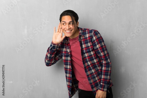 Man over grunge wall listening to something by putting hand on the ear