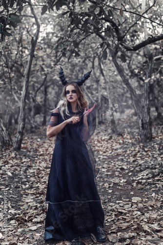 Witch in black robe with horns in a mysterious forest. Sucubus cut her hand in forest
