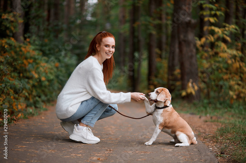 smilng beautiful girl in stylish clothes greeting with a dog, looking at thecaera. full length photo