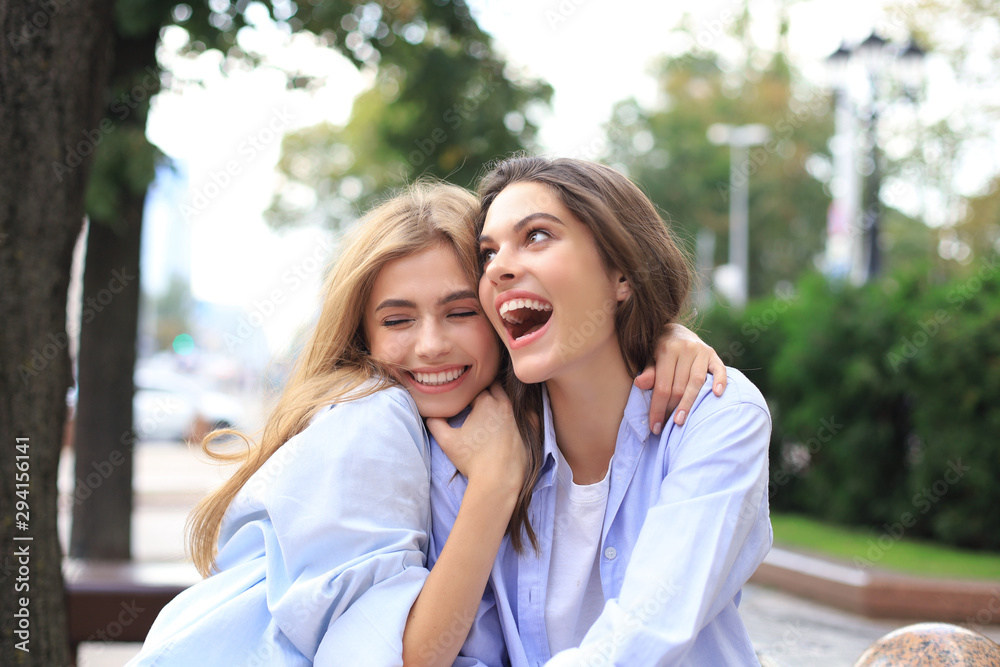 Naklejka premium Two young smiling hipster women in summer clothes posing on street.Female showing positive face emotions.