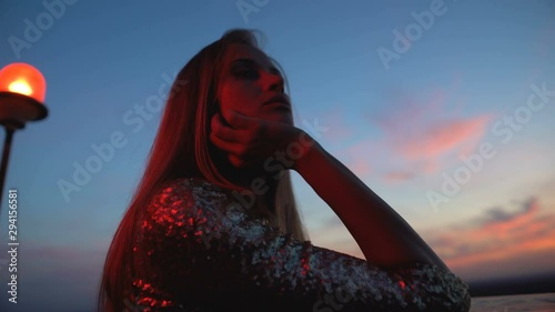 Thoughtful woman in shiny dress standing on roof, feeling lonely at party