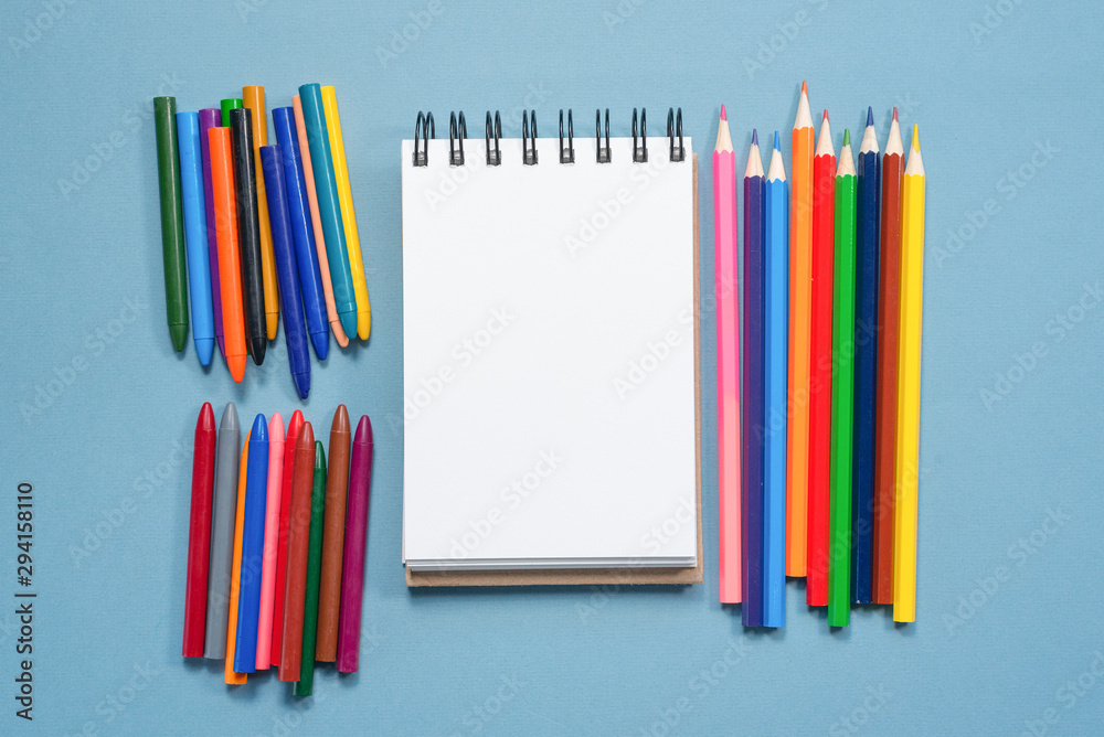 Colorful pencils and blank paper page with copy space on blue background. Colorful pencils and blank paper page with copy space on blue background.