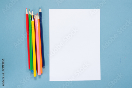Colorful pencils and blank paper page with copy space on blue background.
