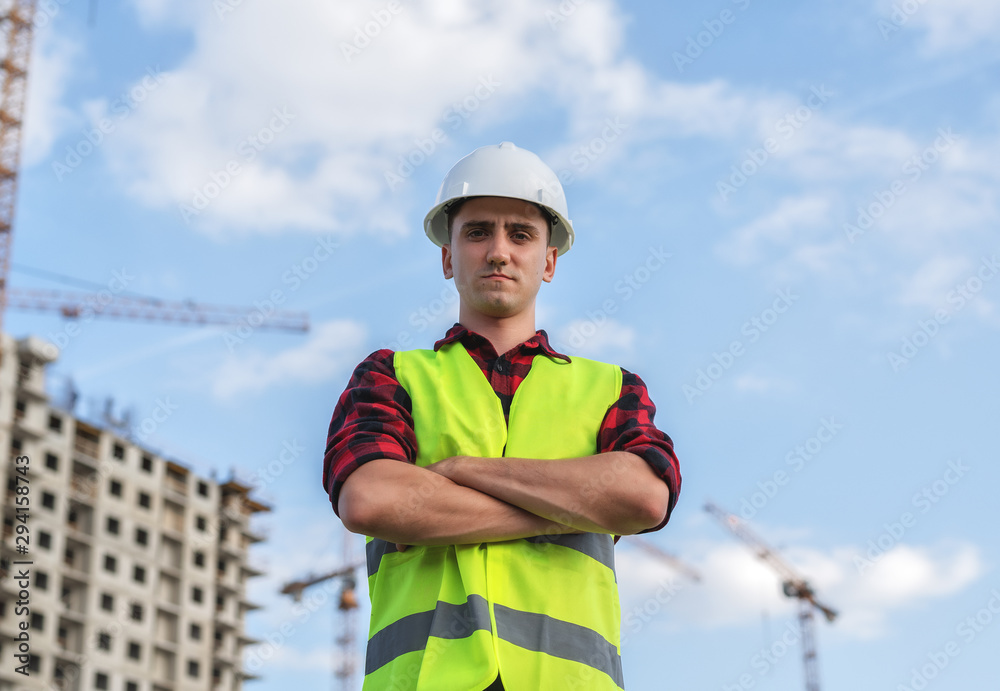 civil engineer in white helmets and a yellow vest on the background of the house under construction.