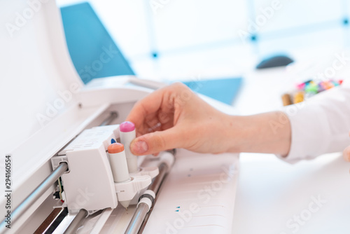 Young woman in printing office insert paper and color pens on plotter