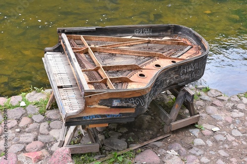 Lithuania, Vilnius - July 2019. Abandoned gran piano, rundown piano by a river bank Vilnia river in Uzupis artists quarter in Vilnius, bohemian. Old piano as an the object of modern art in the Uzupis  photo