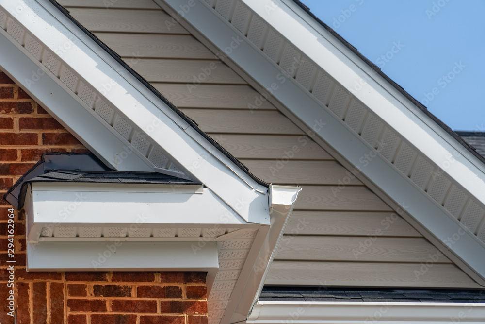 Gable with brick and vinyl siding, white frame gutter guard system, fascia, drip edge, soffit, on a pitched roof attic at a luxury American single family home neighborhood USA Gable with brick and vinyl siding, white frame gutter guard system, fascia, drip edge, soffit, on a pitched roof attic at a luxury American single family home neighborhood USA