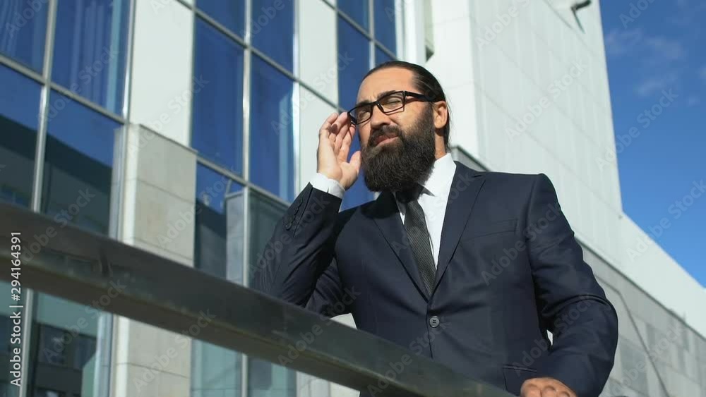 Tired businessman rubbing temples and taking off glasses outdoors, headache