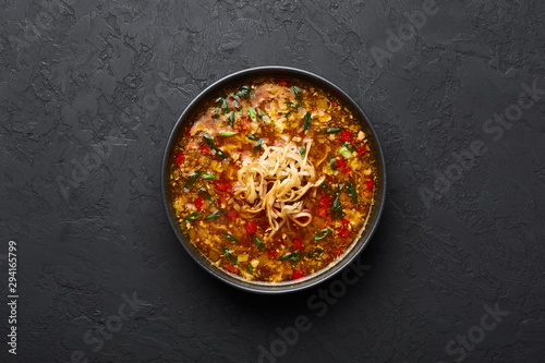 Veg Manchow Soup in black bowl at dark slate background. Vegetarian Manchow Soup is indo-chinese cuisine dish with bell peppers, cabbage, carrot, noodles, chilli, soy sauce and green onion.