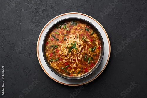 Veg Manchow Soup in black bowl at dark slate background. Vegetarian Manchow Soup is indo-chinese cuisine dish with bell peppers, cabbage, carrot, noodles, chilli, soy sauce and green onion.