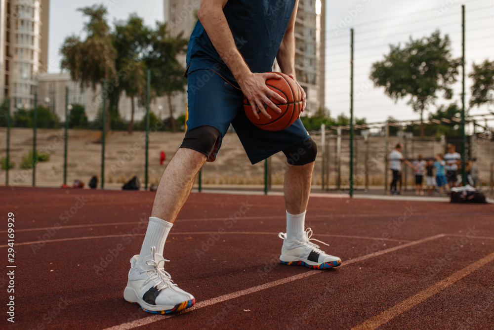 Male basketball player holds a ball, outdoor court
