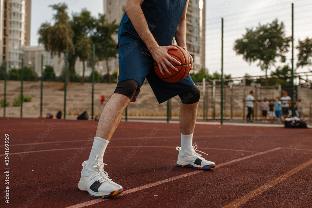 Obraz premium Male basketball player holds a ball, outdoor court