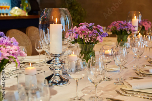 Table setting for guests in a restaurant, on the table forks and glasses for wine - flowers in a vase and a candle on the table