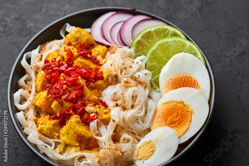 Nan Gyi Thoke in black bowl at dark slate background. Nan gyi Thohk is popular burmese cuisine dish with rice noodles, chicken breasts with spices, eggs, peanuts, lime and red onion. photo