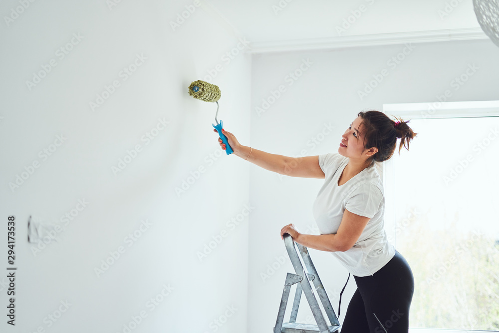 Repair in the apartment, the girl makes repairs in the apartment, paint the walls with a roller, standing on a ladder Repair in the apartment, the girl makes repairs in the apartment, paint the walls with a roller, standing on a ladder