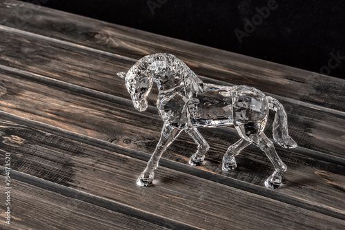 Crystal horse in drops of dew on a wooden shelf