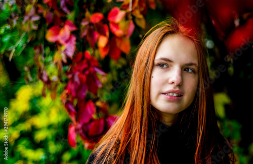 portrait of young teenager redhead girl with long hair on autumn plant leaves background