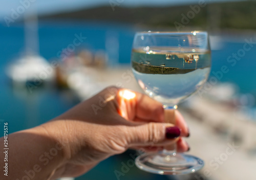 hand with glass of white wine served outside on balcony with sea view