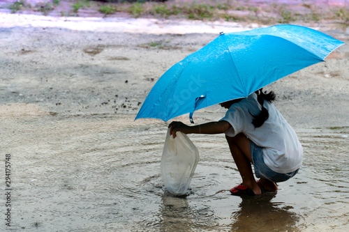 The girls wore white blouses with blue umbrellas playing in the flooded water on the cement floor.
