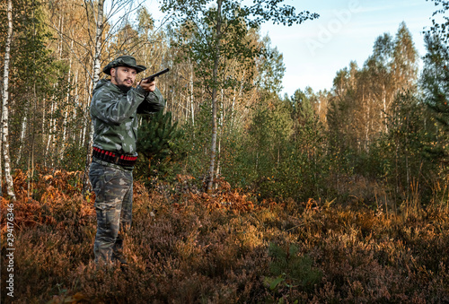 Hunter man in camouflage with a gun during the hunt in search of wild birds or game on the background of the autumn forest. Autumn hunting season. The concept of a hobby, killing.