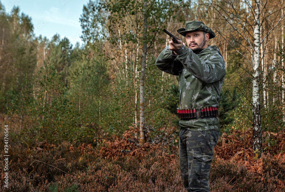 Naklejka premium Hunter man in camouflage with a gun during the hunt in search of wild birds or game on the background of the autumn forest. Autumn hunting season. The concept of a hobby, killing.