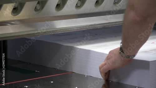 A close up footage of a worker at printing press,putting a stack of sheets in the cutting machine.The machine cuts them into half.Concept of professionalism,job,work. photo