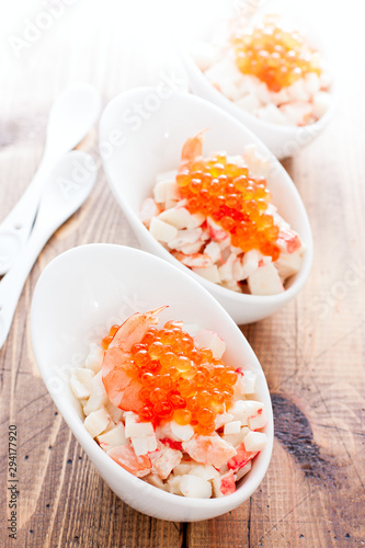 Salad with seafood and red caviar in portioned bowls on a wooden table, selective focus