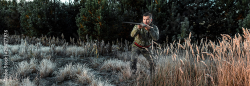 Hunter man in camouflage with a gun during the hunt in search of wild birds or game on the background of the autumn forest. Autumn hunting season. The concept of a hobby  killing.