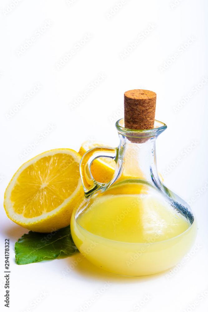 Fresh lemon juice made from ripe yellow Sicilian lemons used for cooking in glass bottle on olive wood plate