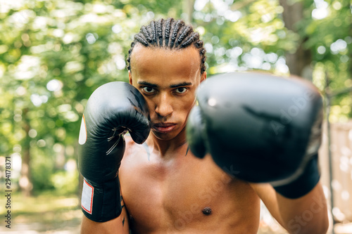 Athlete practicing punches outdoors on sports ground. Close up of a sweated male boxer doing shadow boxing.