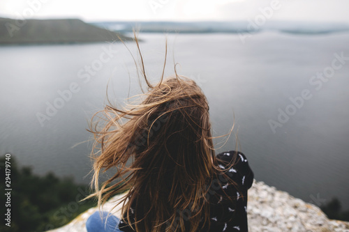 Fotografía Back of hipster girl sitting on top of rock mountain with beautiful view on river