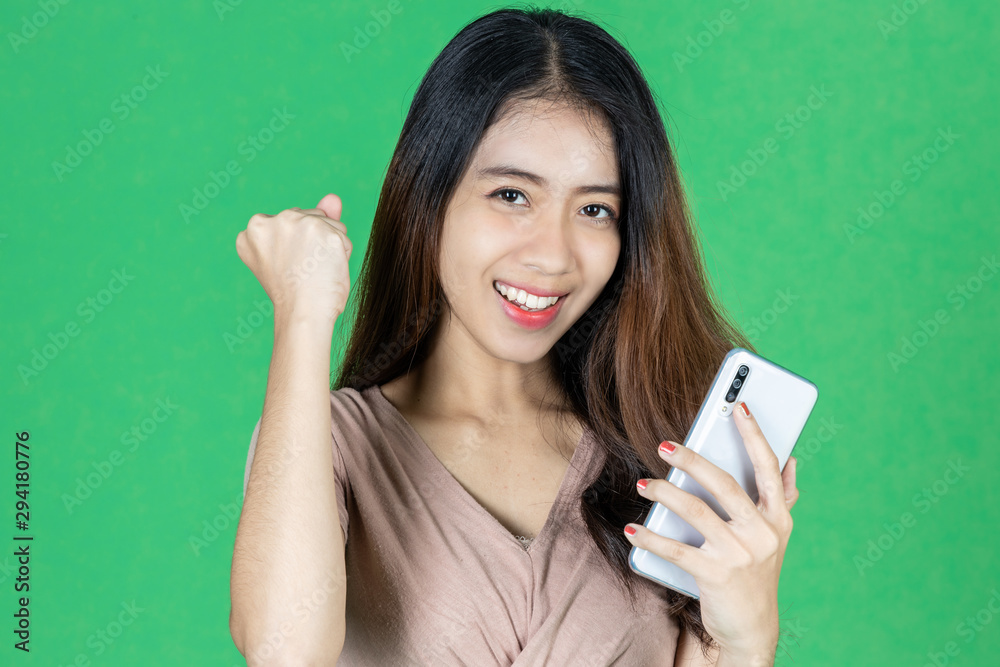 Portrait of success smiling young Asian woman with mobile smart phone raising hands over green isolated background. Skin care concept. Portrait of success smiling young Asian woman with mobile smart phone raising hands over green isolated background. Skin care concept.