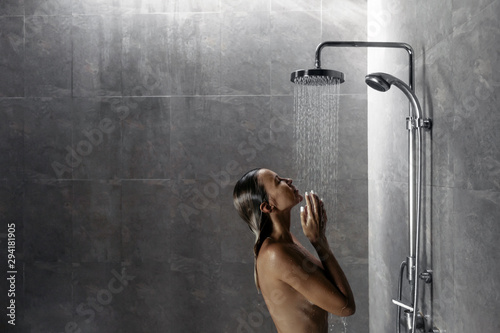 Foto Woman taking shower in dark modern bathroom interior