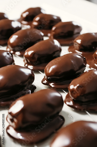 Dates in chocolate, dessert. Confectioner pours chocolate over dessert. Vertical photo.