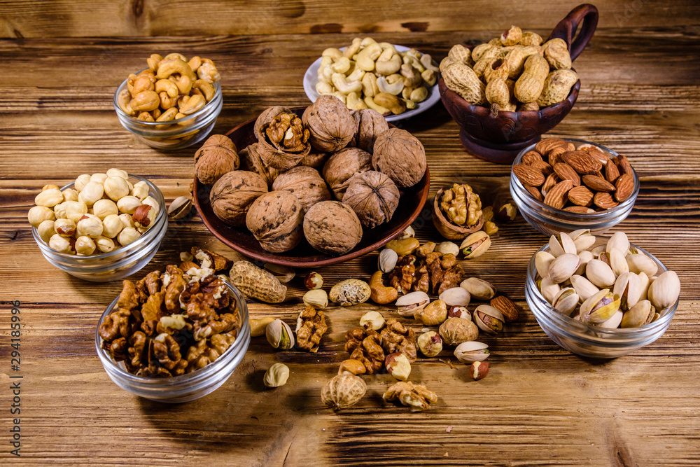 Various nuts (almond, cashew, hazelnut, pistachio, walnut) in bowls on a wooden table. Vegetarian meal. Healthy eating concept